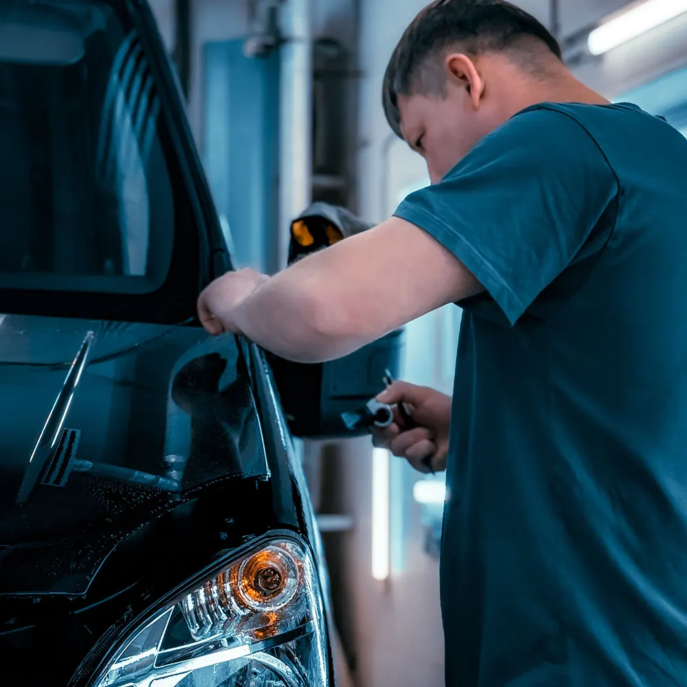Detailer werkt aan de zijkant van een donkere auto in de werkplaats