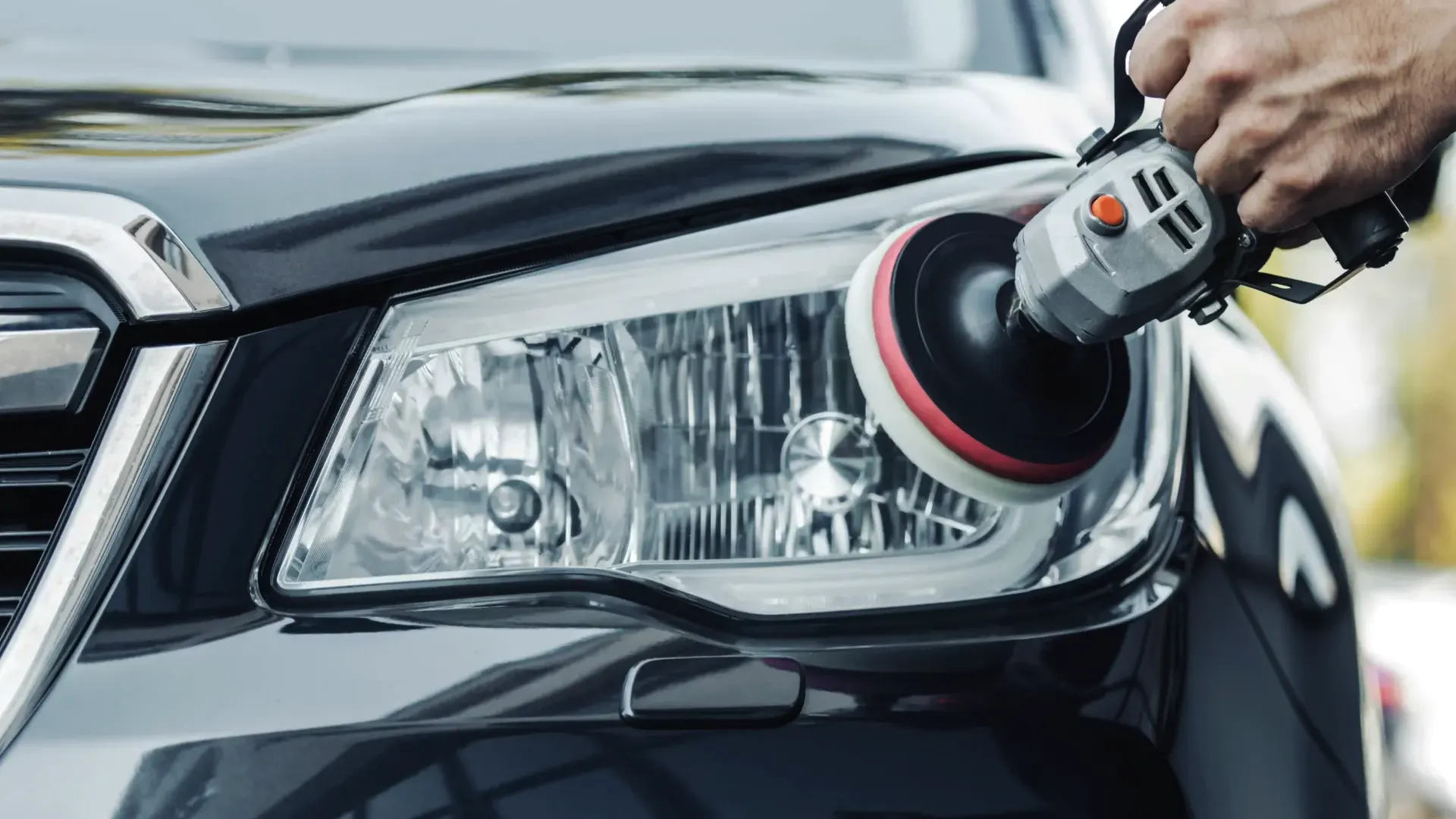 Hand met een polijstmachine op de koplamp van een donkere auto