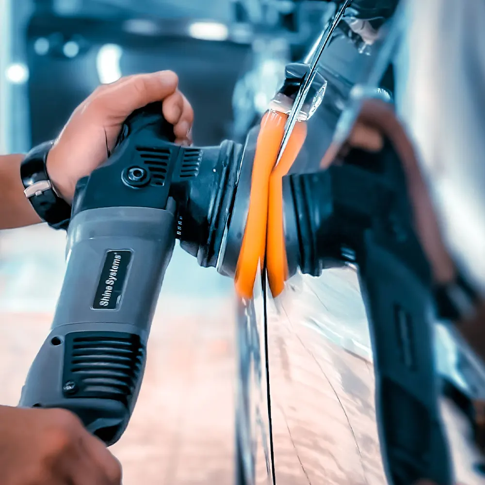 Detailer houdt een polijstmachine met oranje pad tegen een gepolijst paneel